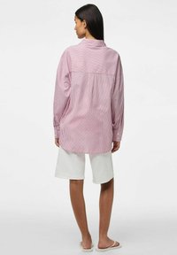 Camicia over size a righe rosse e bianche con maniche lunghe e colletto a bottoni. Abbinata a pantaloni corti bianchi e sandali, vista dalla schiena.