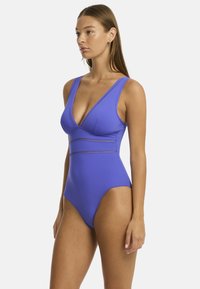 Einteiliger Badeanzug in leuchtendem Lila mit tiefem V-Ausschnitt, breiten Trägern und einer strukturierten Taille mit Ausschnittdetails. Glatte Stoffoberfläche.