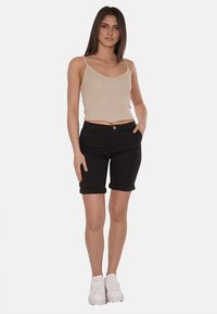 Shorts di denim neri con orli arrotolati, tasche frontali e chiusura con bottone. Abbinati a un top senza maniche a coste beige. Sneakers bianche completano l'outfit.