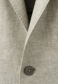 Veste de costume gris clair à motif chevrons avec un revers cranté et un seul bouton gris foncé attaché près du bas au centre.
