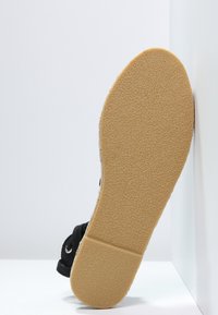 Suola nera della scarpa con superficie texturizzata, caratterizzata da un fondo in gomma marrone chiaro. La parte superiore include componenti in tessuto nero e asole.