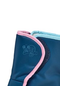 Gros plan sur un tissu bleu avec des bordures rose et bleu clair, présentant un petit graphisme de caméléon sur la partie bleue près d'un patch en Velcro.