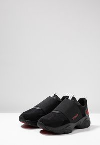 Schwarze Sneaker mit einem Obermaterial aus Mesh, elastischen Riemen, strukturiertem Sohlen und roten Akzenten. Entworfen für Komfort und lässigen Tragekomfort.
