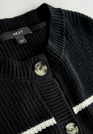 Juodas megztas kardiganas su tekstūruotu raštu, dviem ryškiais mygtukais ir baltais horizontaliais dryžiais ant krūtinės.