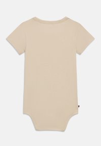 Κοντομάνικο κορμάκι σε ανοιχτό μπεζ χρώμα, κατασκευασμένο από μαλακό βαμβάκι. Διαθέτει στρογγυλή λαιμόκοψη, κούμπωμα με κουμπιά στο κάτω μέρος και μια μικρή ετικέτα με το λογότυπο στο πλάι.