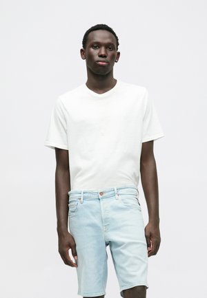 Camiseta de algodón blanca con diseño de escote en V, combinada con pantalones cortos de mezclilla azul claro que cuentan con un cierre de botón y bolsillos laterales.