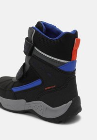 Botte de randonnée imperméable noire et bleue avec semelle grise, bandes velcro et languette en tissu rouge à l'arrière.