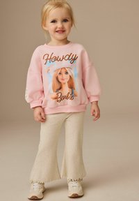 Rosa sweatshirt med "Howdy Barbie" grafik, avslappnad passform, ihopparad med krämfärgade utsvängda byxor och vita sneakers. Slät textur och avslappnad stil.