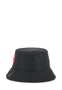 Chapeau seau noir en tissu résistant à l'eau, avec un large bord et un patch logo rouge sur le côté. Texture lisse, forme structurée.