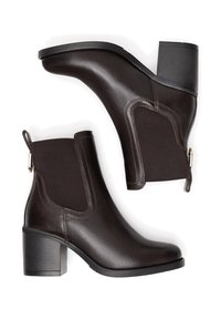 Brūni ādas potīšu zābaki ar masīvu papēdi, elastīgām sānu paneļiem un vilkšanas cilpu. Raksturīga gluda virsma un maigas izšūšanas detaļas.