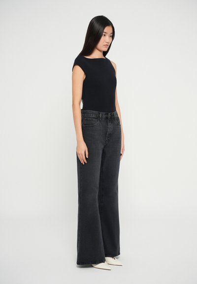 Sort tætsiddende ærmeløs top parret med høj talje flared sorte jeans, der har en let frynset kant og spidse hvide sko.