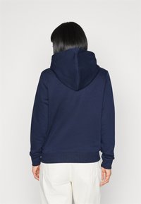 Sudadera azul marino con una gran capucha redondeada, puños y dobladillo de canalé, que muestra una textura suave y lisa.
