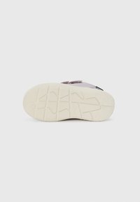 Schuhsohle mit einer strukturierten, hellcremefarbenen Gummibasis; verfügt über ein gemustertes Profil für Griff und Stabilität; weiches lila Obermaterial mit einem Riemen.