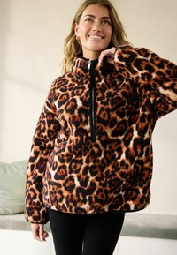 Pull en imprimé léopard en tissu doux et duveteux ; doté d'une fermeture éclair, d'un col montant et d'une coupe décontractée avec des manches longues. Tons orange, noir et marron.