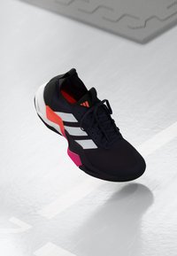 Chaussure de sport noire avec des rayures blanches et des accents roses. Elle possède un dessus texturé, un design à lacets et une semelle rembourrée.