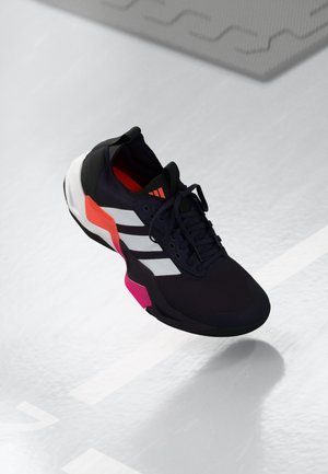Zapatilla deportiva negra con rayas blancas y acentos rosa. Presenta una parte superior texturizada, diseño con cordones y una suela acolchada.