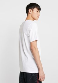 Weißes Baumwoll-T-Shirt mit kurzen Ärmeln, Rundhalsausschnitt und legerem Schnitt. Der Stoff wirkt glatt, ohne sichtbare Muster oder Grafiken.