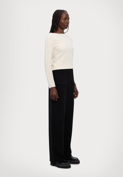Hvid langærmet sweater med firkantet halsudskæring parret med højtaljede, sorte vidde bukser med forlommer og sorte sko.