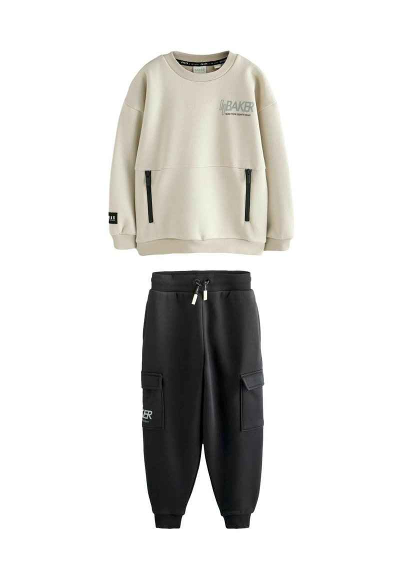 Felpa beige chiaro con due tasche con zip e logo; abbinata a pantaloni jogger neri con due tasche laterali e vita con cordoncino.