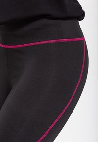 Leggings neri con una cucitura rosa lungo la vita e lungo il lato, realizzati in un materiale morbido e elastico.