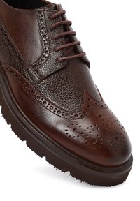Chaussure brogue en cuir marron foncé avec perforations en forme d'aile, tige texturée, bout rond et semelle épaisse en caoutchouc noir.