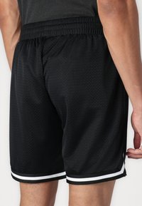 Shorts de sport noirs en tissu en maille respirante, dotés d'une ceinture élastique et de rayures blanches sur l'ourlet.