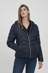 Veste matelassée bleu marine avec un motif en chevrons, fermeture éclair et capuche. Comprend des poches latérales et une texture lisse et brillante.
