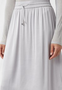 Jupe gris clair avec une taille élastique froncée et un cordon de serrage. Le tissu a une texture lisse, un design fluide et un subtil éclat.