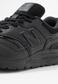 Schwarzer New Balance Sneaker mit strukturiertem Mesh-Zungen, genähten Lederpanelen und geprägtem Logo an der Seite und Sohle.