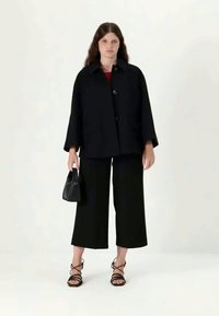 Must mustaga sirge lõikega, suure krae ja nööpidega, kombineeritud laia jalgadega mustade pükstega. Aksessuaarideks on väike must kott ja krepp-kontsadega kingad.