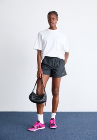 Vit oversized t-shirt, svarta träningsshorts, rosa sneakers med svarta detaljer och en liten svart handväska. Släta texturer, avslappnad design.
