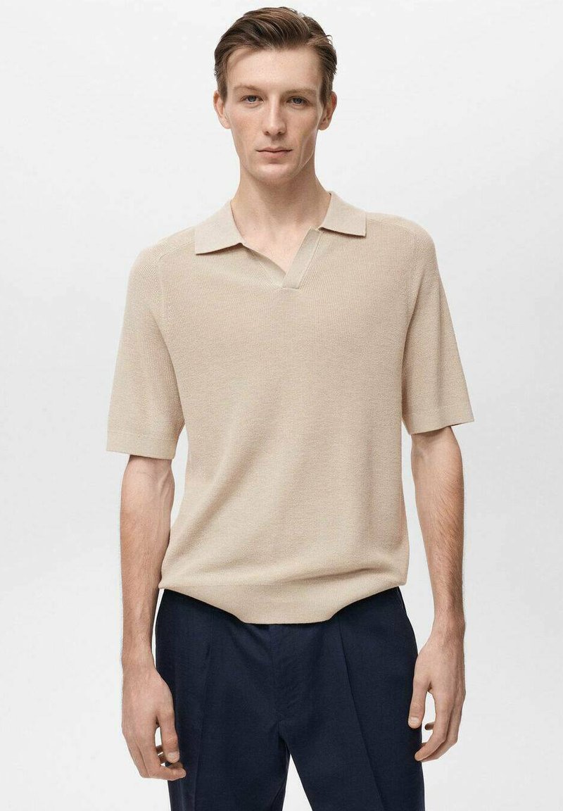 Beige pletená polo košile s krátkým rukávem a výstřihem do V, v kombinaci s tmavě námořnickými kalhotami, které mají hladkou texturu a čisté linie.