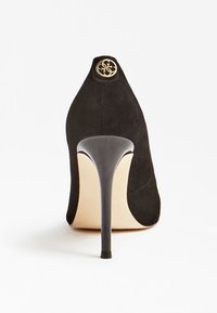 Chaussure à talon haut en daim noir avec un bout pointu, présentant un talon noir brillant et un emblème doré à l'arrière. Doublure intérieure lisse.