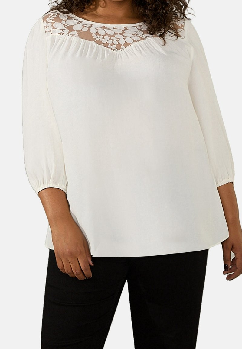 Vit blus med spetsöverdrag vid halsringningen, långa puffärmar och en avslappnad passform. Matchas med svarta åtsittande byxor.