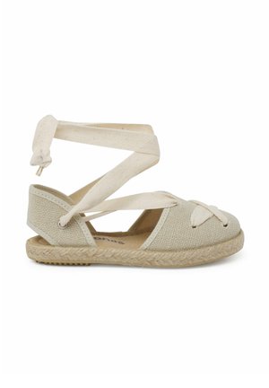 Beige canvas espadrille with crisscross ankle straps, flat jute sole, woven texture, and decorative bow detail on the toe.
