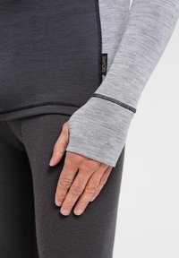 Langærmet bluse med en blanding af mørkegrå og lysegrå stoffer, med tommelhuller og sort syning som detalje, parret med mørkegrå leggings.