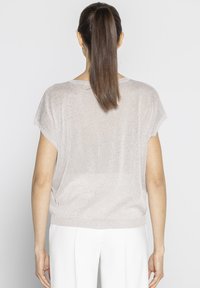 Jasnoróżowa bluzka z krótkim rękawem o luźnym kroju, wykonana z błyszczącego, teksturowanego materiału. Posiada okrągły dekolt oraz prążkowany dół.