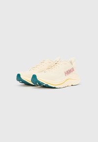 Αθλητικά παπούτσια Hoka σε εκρού χρώμα με τόνους τιρκουάζ και κίτρινο. Διαθέτουν λείο υφασμάτινο πάνω μέρος, ενισχυμένη μεσαία σόλα για απορρόφηση κραδασμών και υφή στην εξωτερική σόλα για καλύτερη πρόσφυση.