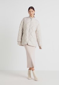 Quiltet beige jakke med blazeren, som har rund krage og oversized fit, parret med en tætsiddende lysebeige nederdel og ankelstøvler.