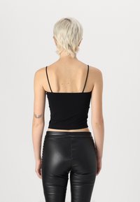 Zwarte, getailleerde tanktop met dunne bandjes, gemaakt van gladde katoen. Gecombineerd met hoog getailleerde, glanzende zwarte leggings.