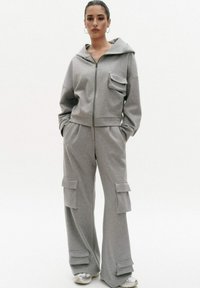 Grijze hoodie en cargobroek set, gemaakt van zachte stof. Kenmerken zijn een ritssluiting aan de voorkant, een voorkantzak, brede pijpen en cargozakken op de broek.