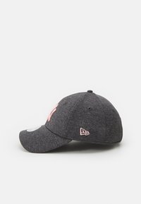 Basebollkeps i mörkgrått tyg, med en rosa broderad logotyp på framsidan och ett litet rosa emblem på sidan. Klippt sidovy.