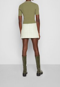 Oliwkowa, prążkowana koszulka polo w połączeniu z fakturowaną, jasnooliwkową mini spódnicą i oliwkowymi, wysokimi do kolan botkami, widok z tyłu.