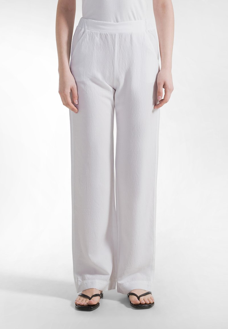 Valkoiset leveälahkeiset housut, jotka on valmistettu kevyestä kankaasta ja joissa on sileä pinta sekä joustava vyötärönauha. Yhdistetty mustiin litteisiin sandaaleihin.