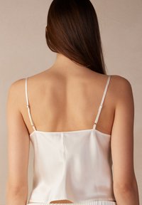 Weißes Satin-Camisole mit dünnen verstellbaren Trägern, das eine glatte Textur und ein einfaches Design aufweist, von hinten betrachtet.