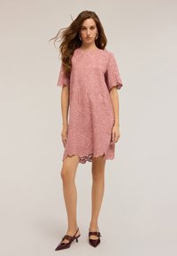 Vestido rosa bordado con mangas cortas, dobladillo en forma de ola y patrones en espiral intrincados. Combinado con tacones burdeos oscuros.