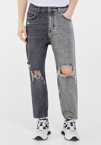 Distressed denim jeans featuring a two-tone design in dark and light gray, with rips near the knees and a loose fit.