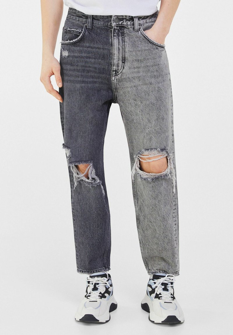 Distressed denim jeans featuring a two-tone design in dark and light gray, with rips near the knees and a loose fit.