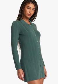 Vestido de color verde azulado con cuello, mangas largas y cierre frontal de botones. Presenta rayas verticales, textura suave y una silueta ajustada.