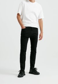 Pantalones skinny de mezclilla negra con un ligero brillo, combinados con una camiseta básica blanca de cuello redondo y zapatillas deportivas negras.